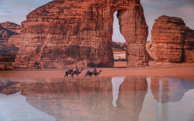 Elephant Rock in AlUla weerspiegeld in water met kamelen bij zonsondergang